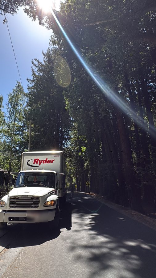 A rented box truck parked on a redwood-lined road at a Bay Area delivery, sun through the trees