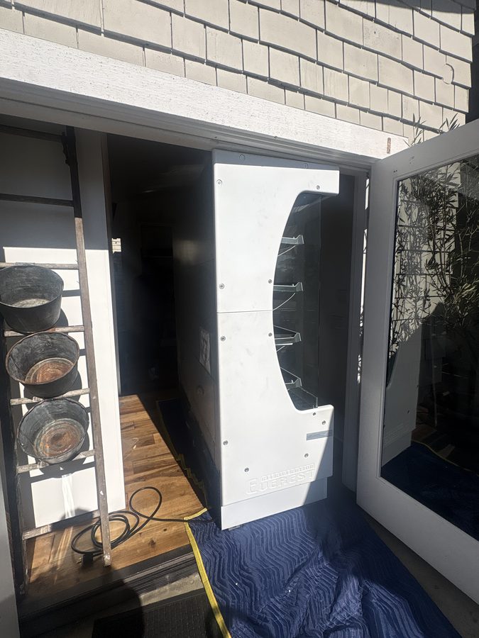 Commercial refrigerated merchandiser at a shop threshold, cabinet and glass intact, before loading on the liftgate