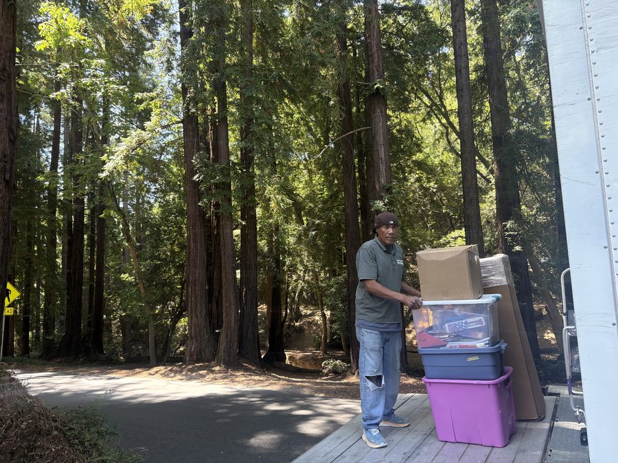 Discount Movers crew member unloading boxes and storage bins from the liftgate at a delivery under redwood trees in Northern California