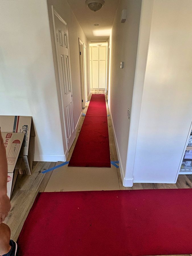 Red carpet runner and taped cardboard sheets laid down the full length of a hallway and entry to protect the flooring during a move