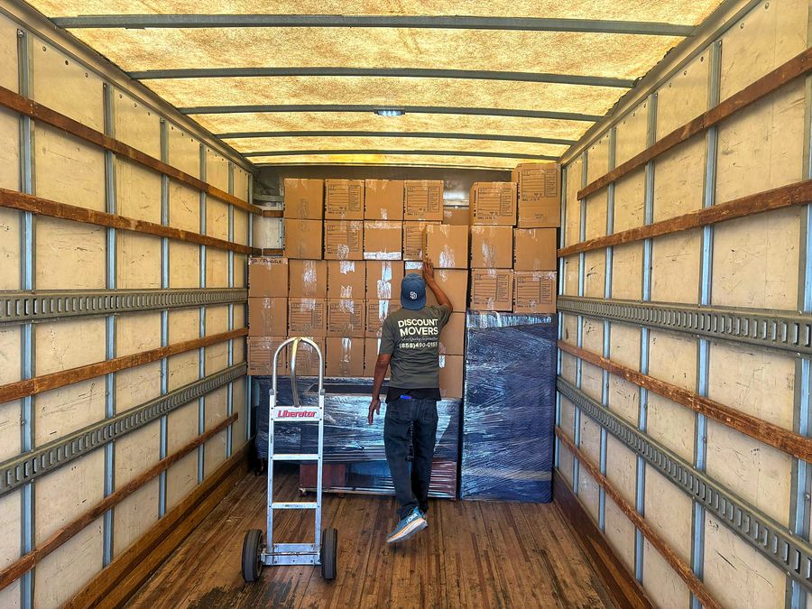 Discount Movers crew member in a branded uniform stacking labeled boxes inside a moving truck