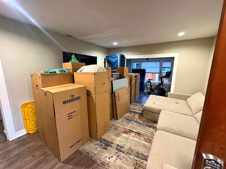 A living room packed for a move: wardrobe cartons and labeled boxes stacked beside the sofa, ready for the crew to load