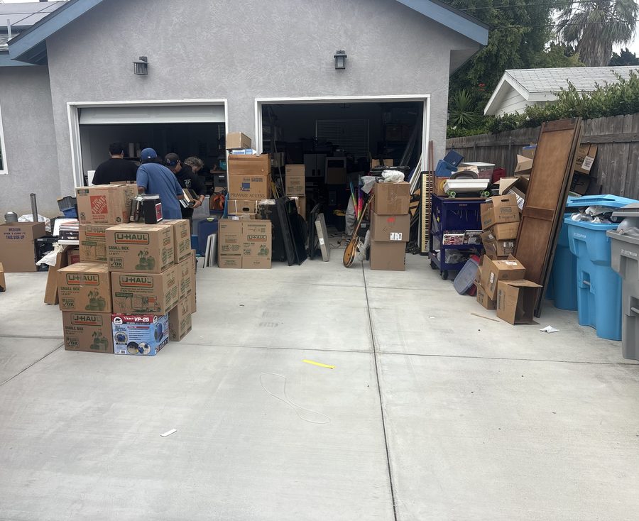 Boxes packed and staged in a driveway during a full pack-out, the Discount Movers crew working in the open garage behind them