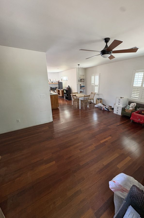 An emptied living room with hardwood floors at the end of a full pack-out, a few chairs left by the window