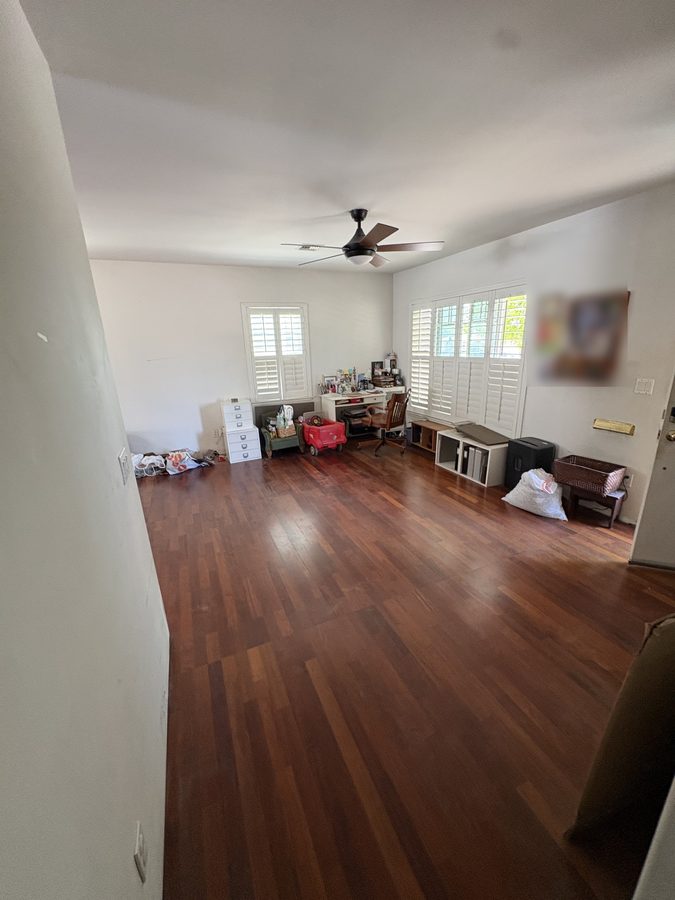 A living room cleared to the hardwood after a pack-and-store job, packing paper and a few last items by the wall