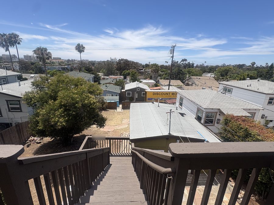 View from a hillside staircase in Bankers Hill over rooftops to the Discount Movers truck parked in the alley below, San Diego towers on the horizon