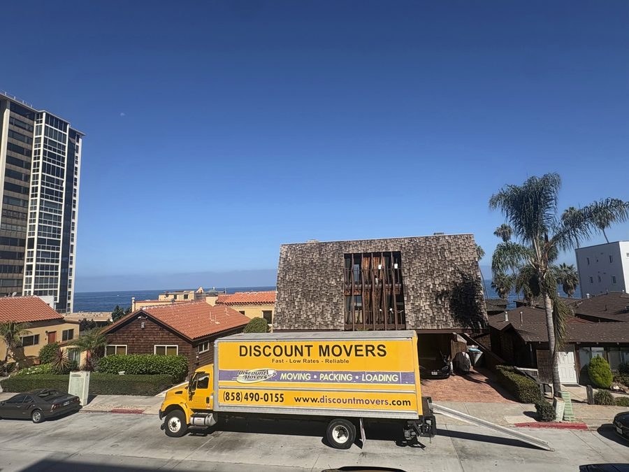Discount Movers truck parked at the curb on a La Jolla street near the Cove, the ocean at the end of the street and the Coast Boulevard tower behind