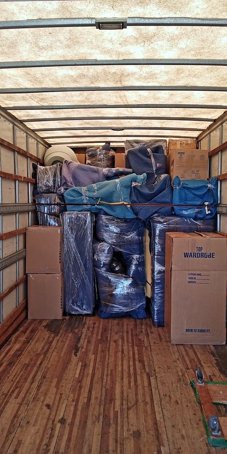 Interior of a Discount Movers truck with furniture blanket-wrapped, shrink-wrapped and stacked to the ceiling, secured behind a load bar