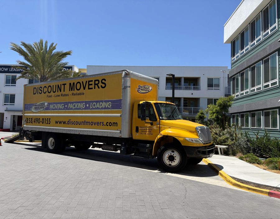 Discount Movers truck outside a new apartment building in Point Loma, the cab door showing the company's DOT and CAL-T numbers